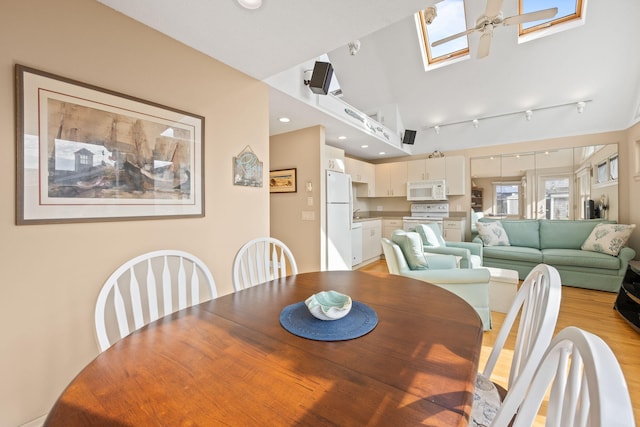 dining space with light hardwood / wood-style floors, vaulted ceiling with skylight, and ceiling fan