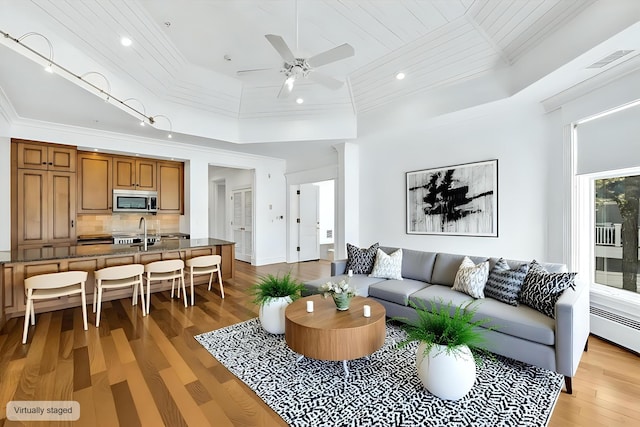 living room featuring sink, ornamental molding, a baseboard heating unit, ceiling fan, and light hardwood / wood-style flooring