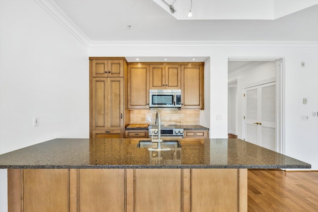 kitchen with sink, tasteful backsplash, dark stone countertops, ornamental molding, and a large island