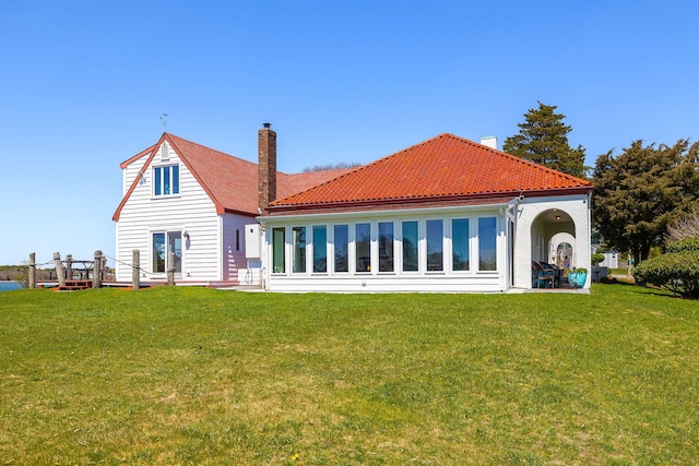 back of house with a yard, a tile roof, and a chimney