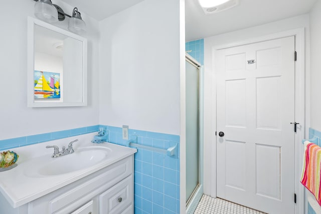 bathroom with tile walls, vanity, tile patterned floors, a stall shower, and wainscoting