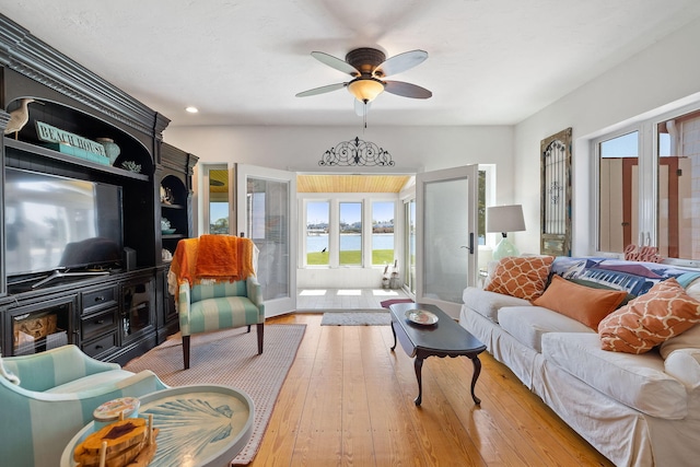 living area with a ceiling fan, a water view, french doors, and a healthy amount of sunlight