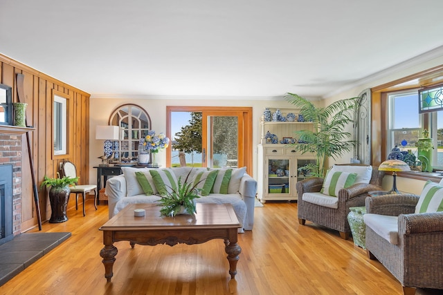 living area featuring light wood finished floors, ornamental molding, and a brick fireplace