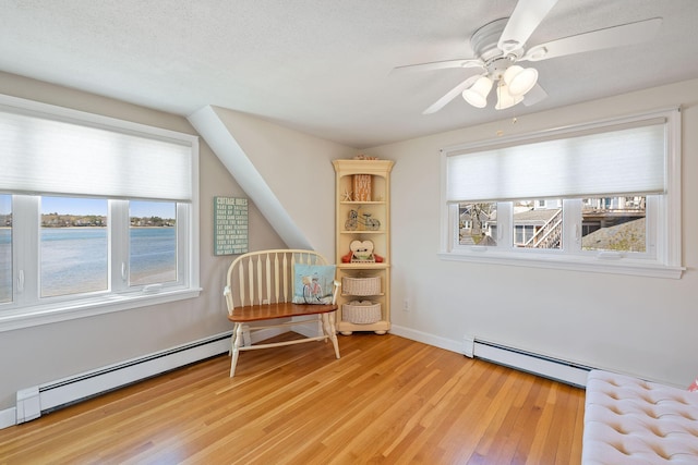 living area with a baseboard heating unit, light wood finished floors, ceiling fan, baseboard heating, and baseboards