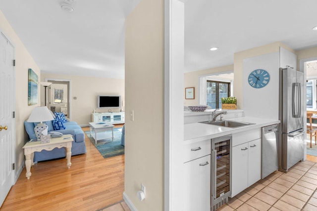 kitchen featuring beverage cooler, a sink, white cabinetry, light countertops, and appliances with stainless steel finishes