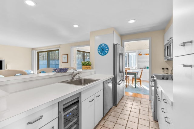 kitchen featuring stainless steel appliances, light countertops, white cabinets, a sink, and beverage cooler