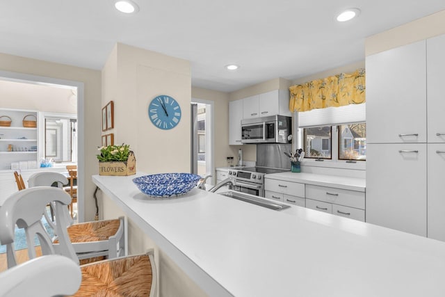 kitchen featuring light countertops, recessed lighting, stainless steel microwave, and a sink