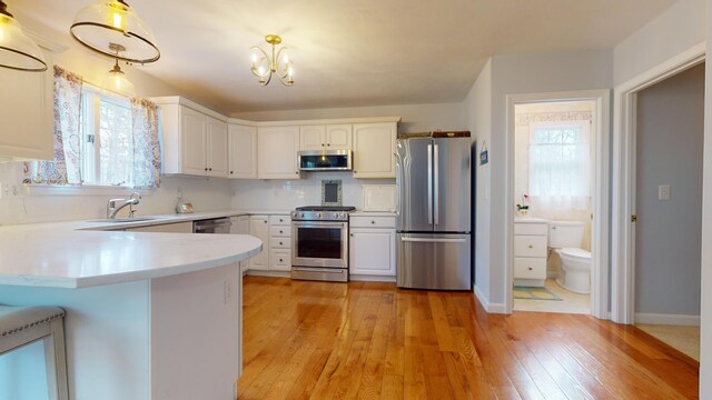 kitchen with pendant lighting, sink, white cabinetry, stainless steel appliances, and kitchen peninsula