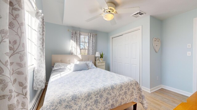 bedroom featuring baseboard heating, ceiling fan, light hardwood / wood-style floors, and a closet