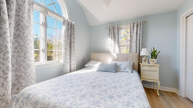 bedroom featuring multiple windows, vaulted ceiling, ceiling fan, and light wood-type flooring