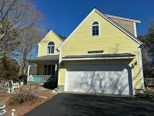 traditional home featuring a porch, an attached garage, and aphalt driveway