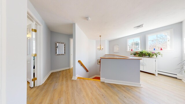 kitchen with white cabinetry, hanging light fixtures, a baseboard radiator, and light hardwood / wood-style floors