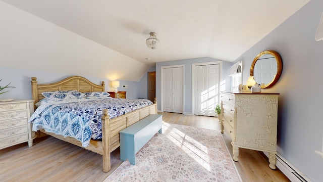 bedroom with multiple closets, a baseboard radiator, vaulted ceiling, and light wood-type flooring