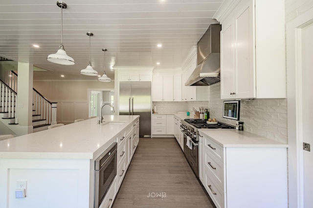 kitchen featuring pendant lighting, wall chimney exhaust hood, white cabinetry, built in appliances, and sink