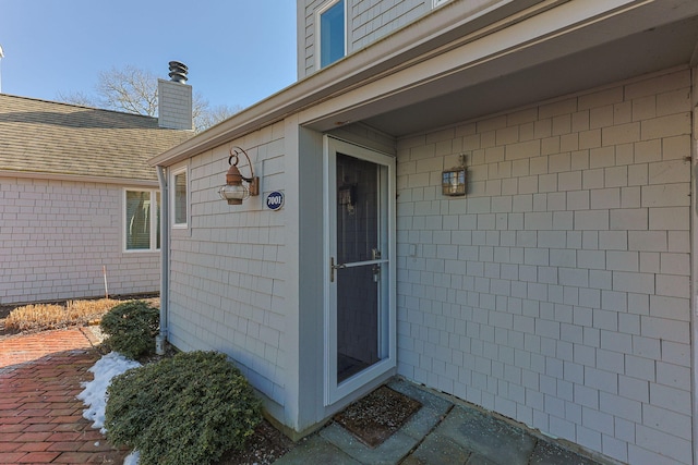 view of exterior entry with roof with shingles