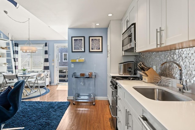 kitchen featuring backsplash, appliances with stainless steel finishes, a sink, baseboards, and white cabinetry