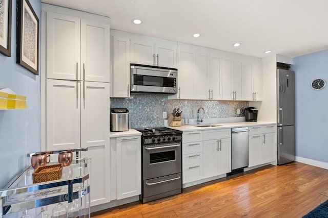 kitchen featuring decorative backsplash, appliances with stainless steel finishes, a sink, light countertops, and white cabinetry