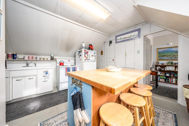 kitchen featuring lofted ceiling, sink, white appliances, a breakfast bar area, and white cabinetry