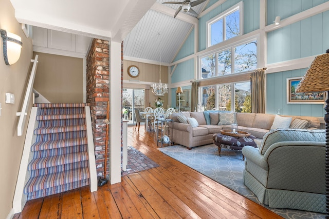 living area featuring ceiling fan with notable chandelier, high vaulted ceiling, stairs, and wood-type flooring