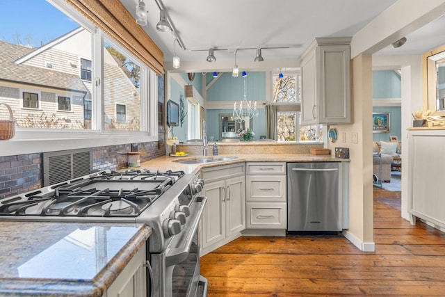 kitchen with a notable chandelier, a sink, backsplash, hardwood / wood-style floors, and appliances with stainless steel finishes