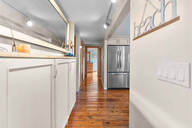 kitchen with light stone counters, white cabinets, rail lighting, hardwood / wood-style flooring, and stainless steel fridge