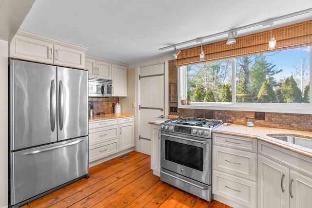 kitchen with light wood-type flooring, light stone counters, backsplash, white cabinetry, and stainless steel appliances