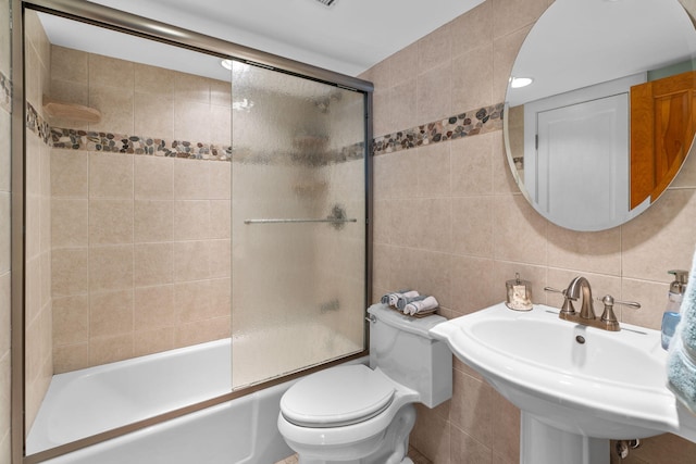 bathroom featuring toilet, a sink, tasteful backsplash, tile walls, and enclosed tub / shower combo