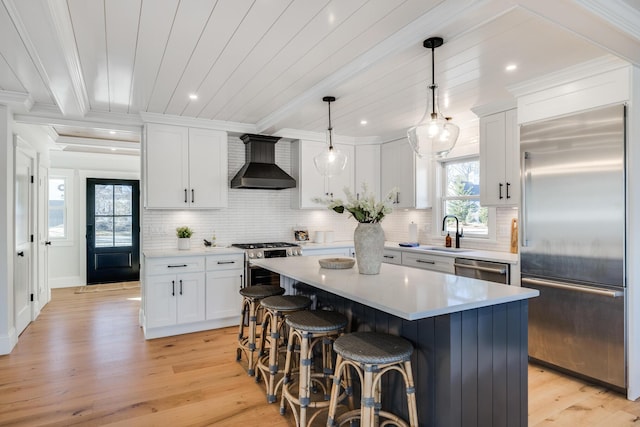 kitchen with a sink, stainless steel appliances, wall chimney range hood, white cabinetry, and backsplash