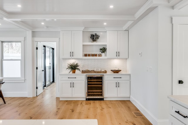 bar with wine cooler, light wood finished floors, decorative backsplash, ornamental molding, and baseboards