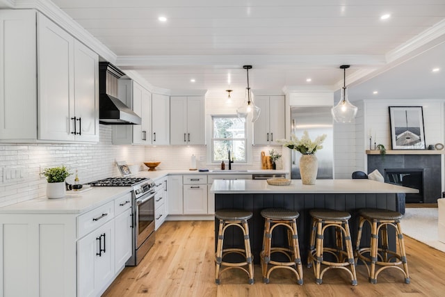 kitchen featuring a sink, wall chimney range hood, appliances with stainless steel finishes, a kitchen bar, and crown molding