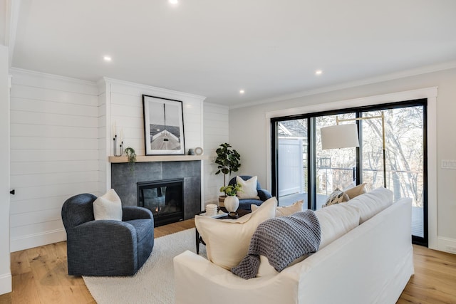 living room with light wood-type flooring, ornamental molding, and a tiled fireplace