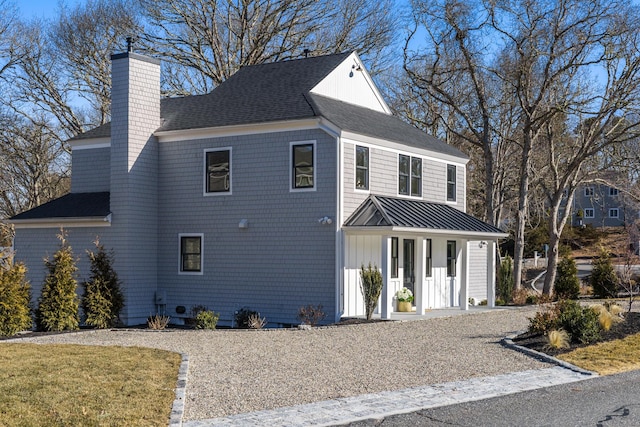 view of front facade with metal roof, a porch, roof with shingles, a standing seam roof, and a chimney