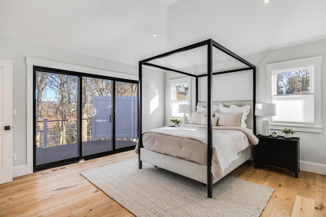 bedroom featuring vaulted ceiling, multiple windows, wood finished floors, and access to exterior