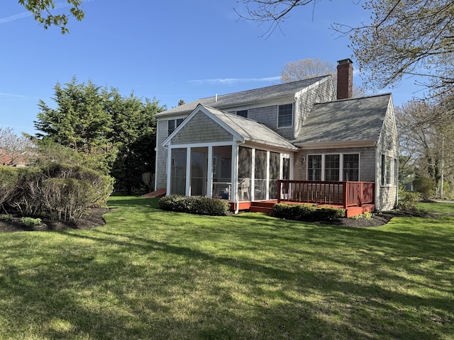 back of property with a shingled roof, a wooden deck, a sunroom, a chimney, and a yard