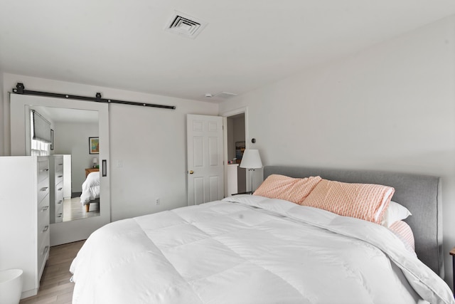 bedroom with light wood finished floors, a barn door, and visible vents