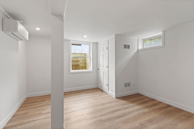 basement featuring light wood finished floors, a wall mounted air conditioner, visible vents, and baseboards