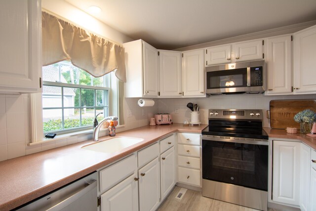 kitchen featuring white cabinets, decorative backsplash, stainless steel appliances, and a sink