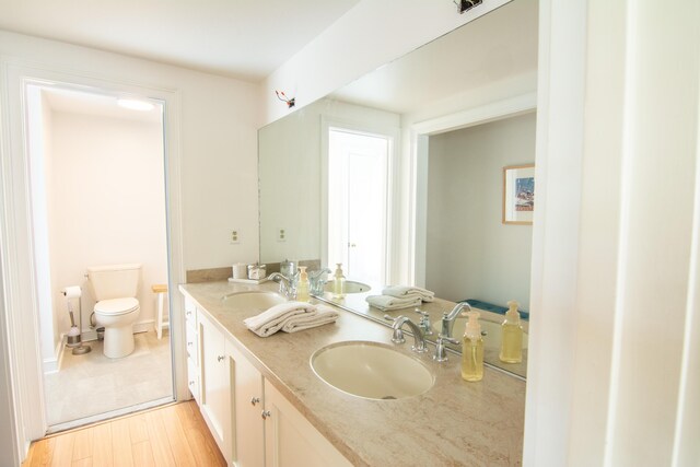 full bath featuring double vanity, wood finished floors, a sink, and toilet