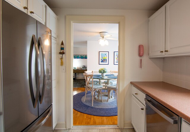 kitchen with appliances with stainless steel finishes, light wood-type flooring, white cabinets, and tasteful backsplash