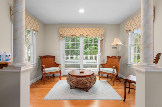 living area featuring light wood-type flooring, decorative columns, and baseboards