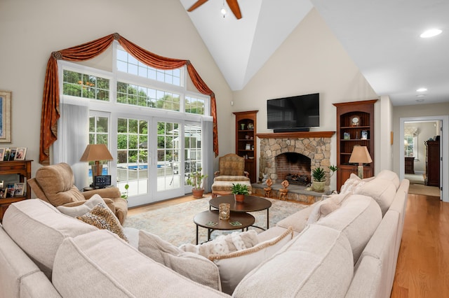 living area featuring high vaulted ceiling, a stone fireplace, ceiling fan, and light wood finished floors