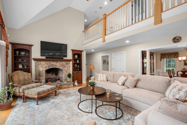 living area with decorative columns, a fireplace, an inviting chandelier, wood finished floors, and high vaulted ceiling