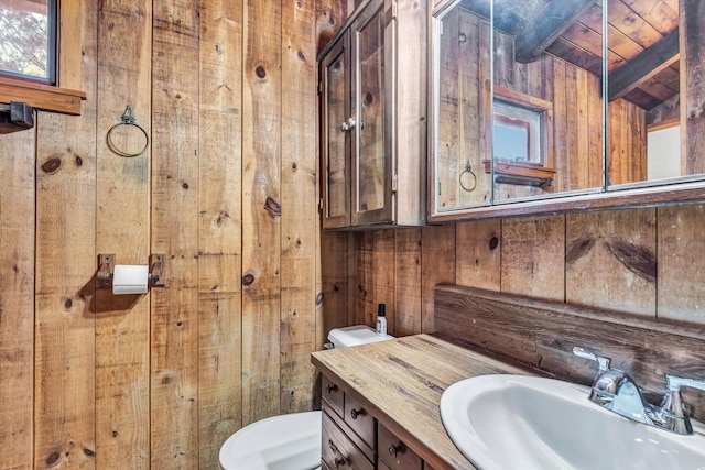 half bathroom featuring plenty of natural light, wood walls, vanity, and toilet