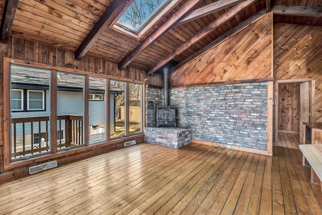 unfurnished living room featuring a wood stove, wood walls, a skylight, and visible vents