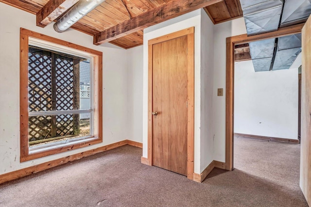 unfurnished bedroom featuring wood ceiling, carpet, baseboards, and beamed ceiling