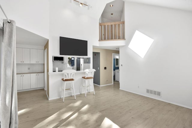 interior space featuring tasteful backsplash, white cabinetry, high vaulted ceiling, kitchen peninsula, and a breakfast bar area