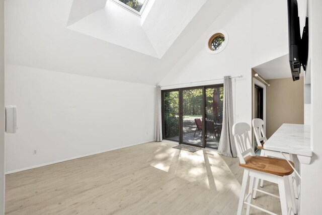 interior space featuring light wood-type flooring, high vaulted ceiling, and a skylight