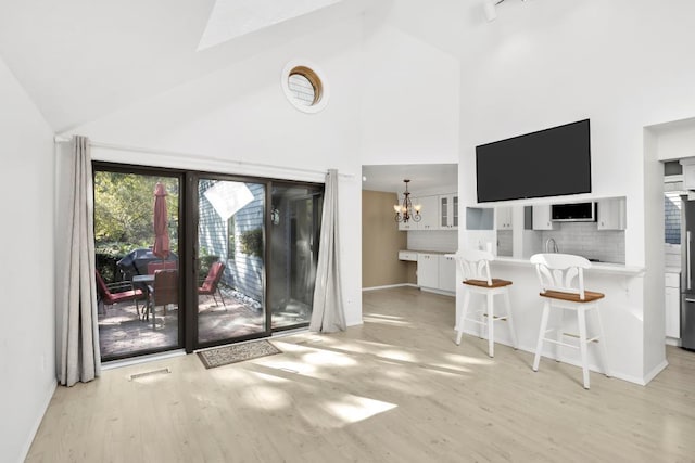 unfurnished living room featuring light hardwood / wood-style flooring, high vaulted ceiling, and a notable chandelier