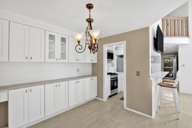 kitchen featuring decorative backsplash, white cabinets, decorative light fixtures, light wood-type flooring, and stainless steel range with gas stovetop