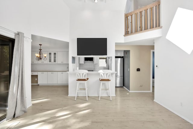 kitchen featuring backsplash, white cabinetry, a towering ceiling, a breakfast bar, and stainless steel refrigerator